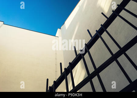 Fragment of yellow facade of the house and the stylish, modern iron gate against the blue sky Stock Photo