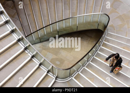 Woman carrying shopping bag up a triangular spiral staircase in London