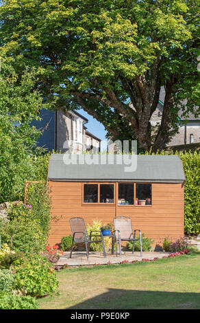 A Dutch style wooden garden shed with patio and two chairs 