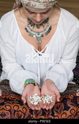 High angle view of woman wearing white blouse headscarf sitting on floor, holding seashells. Stock Photo