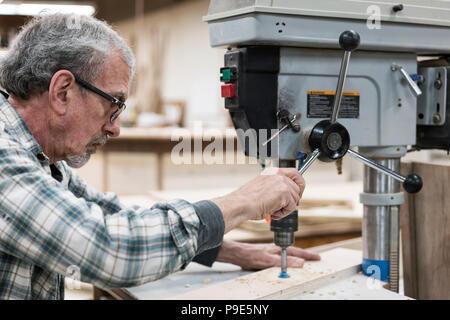 A senior man with glasses and beard in a woodworkers shop, using a machine. Stock Photo
