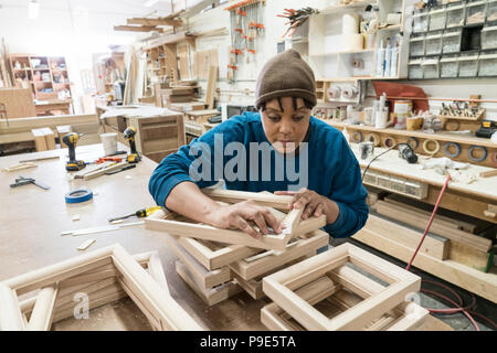 A Black woman carpenter working on a cabinet project in a large woodworking shop. Stock Photo