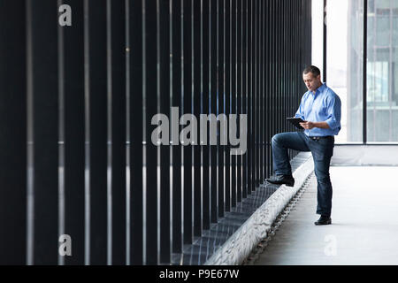 A Caucasian male architect standing by a wall of windows, using a digital tablet. Stock Photo