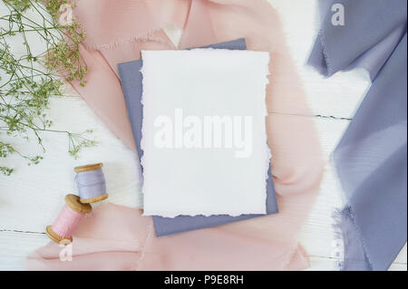 White blank card on a background of pink and blue fabric on a white background. Mockup with envelope and blank card. Flat lay. Top view Stock Photo