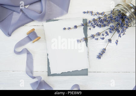 White blank card on a background of blue ribbon with lavender flowers on a white background. Mockup with envelope and blank card. Flat lay. Top view Stock Photo