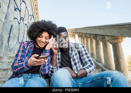 couple enjoying the music and the modern technology with phone together in friendship. black race african with afro ethnic hair. smiles and having fun Stock Photo