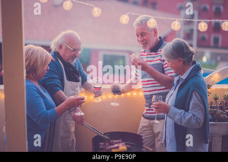 senior adult people group in leisure activity doing barbeque bbq on the rooftop terrace at home with mountain view. meal and wine for two men and two  Stock Photo