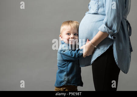 Young toddler boy holds mummy's baby bump and cuddles it Stock Photo