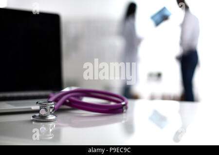 Laptop and stethoscope on the desk , doctors standing in the background Stock Photo