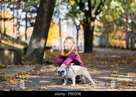 Beautiful redhead girl enjoying autumn day in a park with her French bulldog puppy. Stock Photo