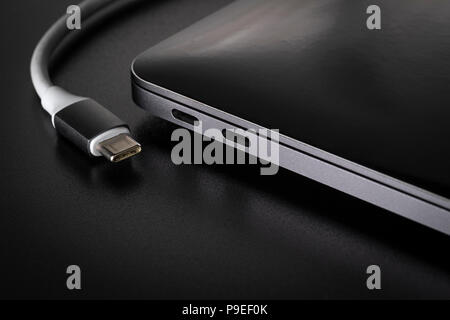 One USB type C cable disconnected from laptop computer on black background Stock Photo
