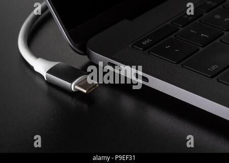 One USB type C cable disconnected from laptop computer on black background Stock Photo