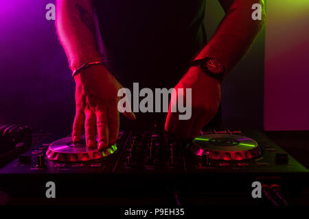 Dj mixing on turntables with color light effects. Soft focus on hand. Close-up. Stock Photo