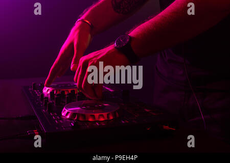 Dj mixing on turntables with color light effects. Soft focus on hand. Close-up. Stock Photo