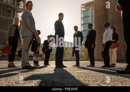 Business people looking at camera. Office going people standing on a busy street with sun flare in the background. Stock Photo