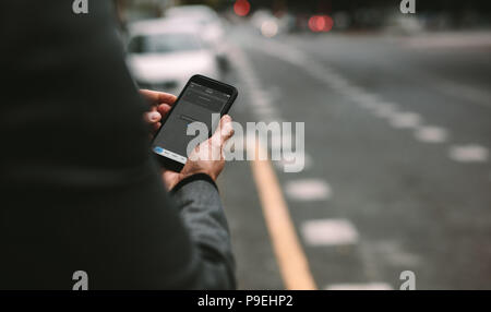Close up of mature man using ride sharing application on smartphone for ordering taxi on city street. Stock Photo