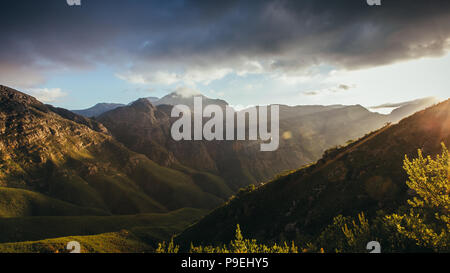 Sun rays from right over the hill, lighting up the mountain valley. Mountains and cloudy sky sunset in Jonkershoek nature reserve. Stock Photo