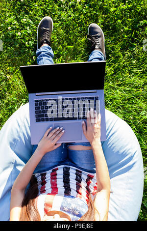Top view. Woman working on laptop pc computer with blank black empty screen to copy space in park on green grass sunshine lawn outdoors. Stock Photo