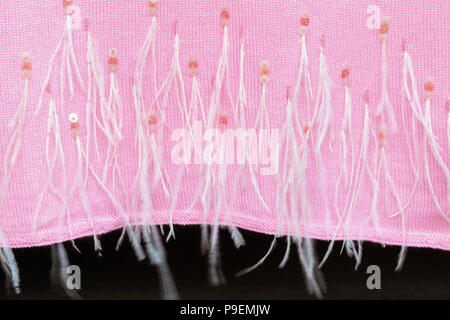 Big soft knitted pink cashmere scarf decorated with sequins and ostrich feathers waving on wooden hanger at wardrobe. Stylish delicate handmande woole Stock Photo