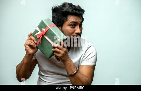 A brutal bearded man in a white T-shirt is holding a present. curious male listening to what in gift box. close up portrait. isolated white background Stock Photo