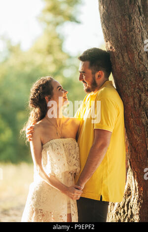Young enamored couple smiles, hugs and holds hands in forest against background of tree. Stock Photo