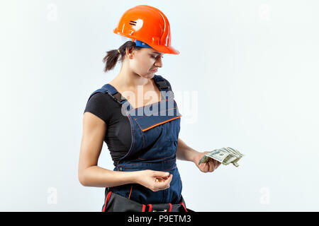 Young woman builder in a helmet holding banknotes. She has a displeased face. Stock Photo