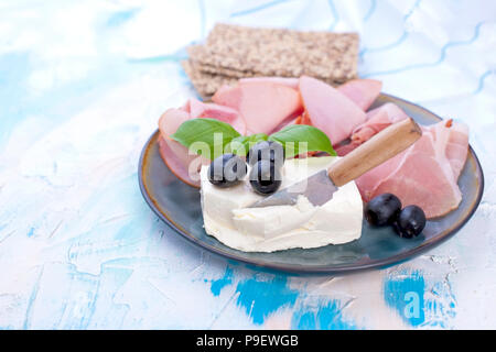 Cheese and ham with olives on a gray plate. White background with blue divorces. Knife for cheese. Dry Breadstones. Free space for text or a postcard Stock Photo