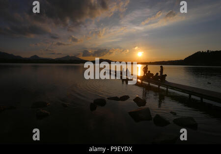 12 July 2018, Germany, Fuessen: Holidaymakers enjoy the sunset on a pier at Hopfensee lake. Photo: Karl-Josef Hildenbrand/dpa Stock Photo