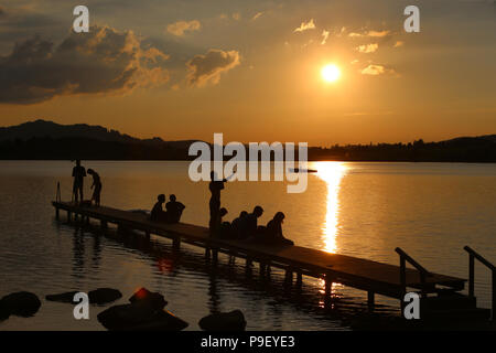 12 July 2018, Germany, Fuessen: Holidaymakers enjoy the sunset on a pier at Hopfensee lake. Photo: Karl-Josef Hildenbrand/dpa Stock Photo