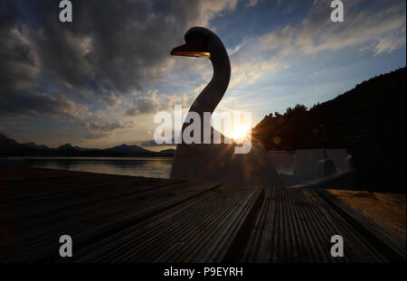 12 July 2018, Germany, Fuessen: A pedal boat in the shape of a swan is at the waterfront of the Hopfensee lake during sunset. Photo: Karl-Josef Hildenbrand/dpa Stock Photo