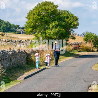 Aberlady, East Lothian, Scotland, United Kingdom, 18th July 2018. UK Weather: A beautiful sunny morning in the coastal village of Aberlady on the Firth of Forth. A woman takes three young children out for a walk along a quiet road Stock Photo