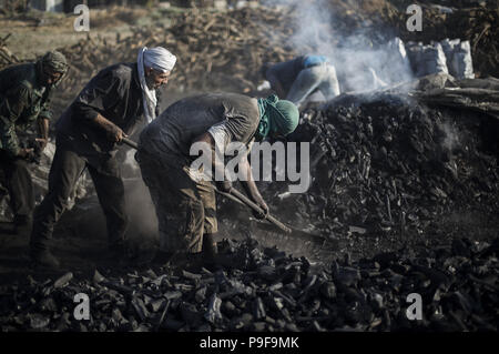 July 18, 2018 - Gaza City, The Gaza Strip, Palestine - Palestinian workers extract charcoal from sand at the Al Hattab production facility, east of the Jabaliya refugee camp, northern Gaza City, Gaza Strip. After harvesting the trees, workers form wood in the form of a pyramid buried under the sand. The pyramid is placed on fire, and burns inside for several days. During this period, workers must control the burning process by regularly moistening the pyramid with water. Workers can then harvest and clean raw coal. Coal is usually used by Palestinians for practical purposes, such as cooking an Stock Photo