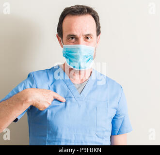 Senior doctor man using mask with surprise face pointing finger to himself Stock Photo