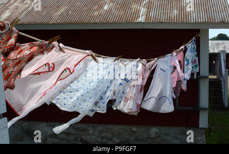 Vintage aprons blowing in the breeze on an old-fashioned clothesline hanging on a shed on a summers day. Vintage fabrics. Stock Photo