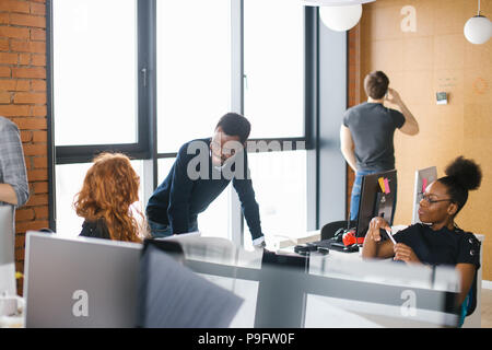 nice african office assistants are greeting Caucasian woman with long red hair while man on the background of the picture is having serious conversati Stock Photo