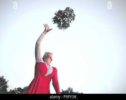 Bespectacled Blonde Teen Majorette Girl with Pom-poms Outdoors in Red Dress Stock Photo