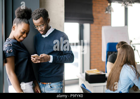 young african attractive woman and man standing in the corner of office and looking at the screen of cell phone in the loft office Stock Photo