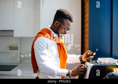 closeup side view portrait of african office worker holding mobile phone and working with printer at workplace. printing on the copy machine. using co Stock Photo