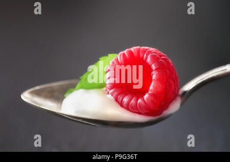 Close-up on a jspoon of yougurt with juisy raspberry nd mint leaf on top on dark gray background Stock Photo