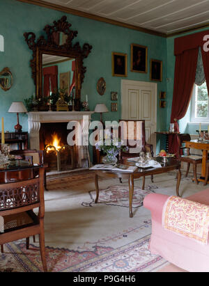 Lighted fire in fireplace in a turquoise country drawing room with antique furniture with a large patterned rug Stock Photo