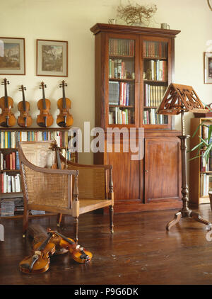 Antique bookcase and colonial cane chair in music room with wooden floor and collection of violins Stock Photo