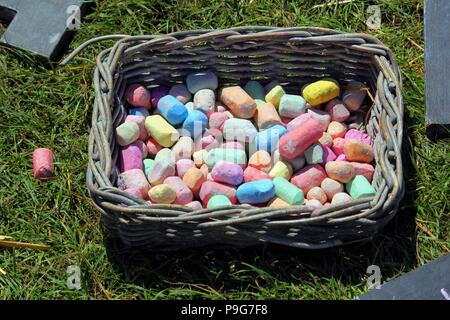 Basket outside on the grass,containing lots of pieces of multi colored colourful chalk, red, blue, orange,yellow, green and pink Stock Photo