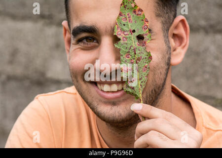 Happy young man holding a ruin leaf in front of face at outdoor area Stock Photo