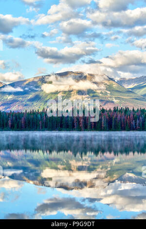 Morning sun and low clouds cover the Rocky Mountains at Annette Lake in Jasper National Park with dreamy reflections of Majestic Mountain off its wate Stock Photo