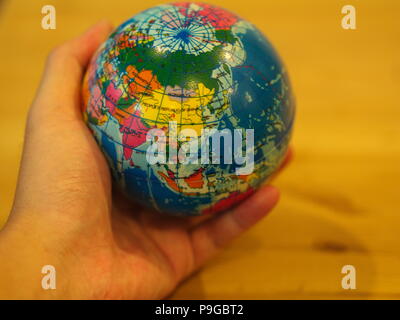 Close Up Hand holding a Mini Globe with Wooden Table Background Stock Photo