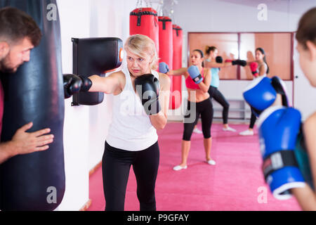 vigorous mature female is doing exercises with punching bag in sporty gym Stock Photo