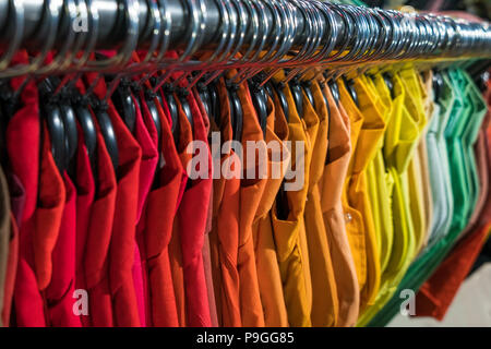 Male men’s shirts sorted in color order on hangers on a thrift shop or wardrobe closet rail Stock Photo