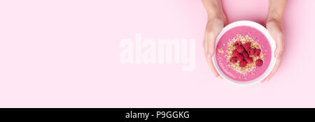 Woman's hands holding raspberries smoothie bowl on pink background. Top view, copy space. Banner for website with copy space. Stock Photo