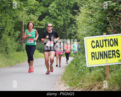 A 'caution runners' sign with female runners taking part in a road race Stock Photo