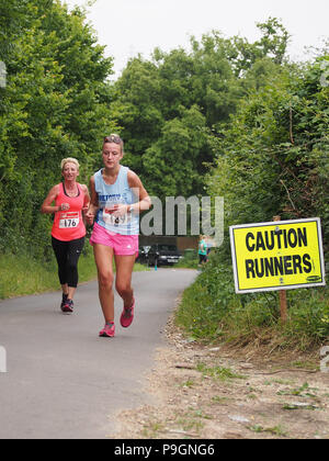 A 'caution runners' sign with female runners taking part in a road race Stock Photo